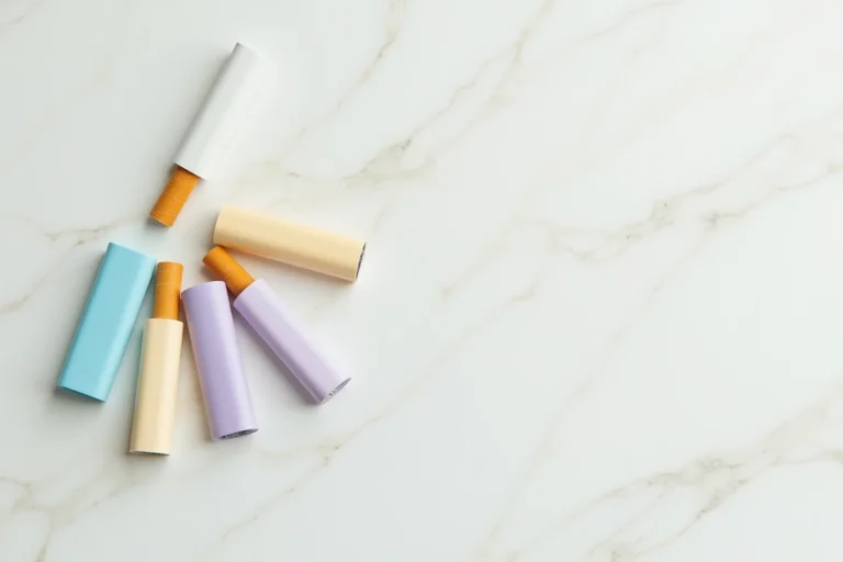Plusieurs paquets de cigarettes Vogue de couleurs pastel différentes disposés en éventail sur un marbre blanc, illustrant les variantes de la gamme